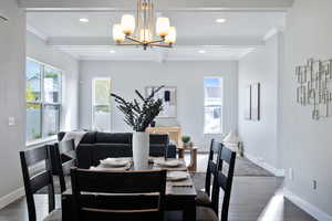 Dining space with beam ceiling, dark wood-type flooring, crown molding, and an inviting chandelier