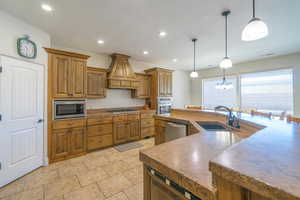 Kitchen featuring an island with sink, sink, pendant lighting, custom exhaust hood, and appliances with stainless steel finishes