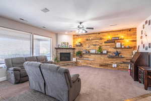 Living room featuring wooden walls, ceiling fan, a stone fireplace, and carpet