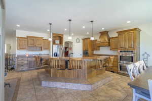 Kitchen featuring custom range hood, a breakfast bar, a large island, appliances with stainless steel finishes, and decorative light fixtures