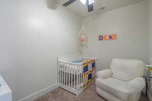 Carpeted bedroom featuring a crib, lofted ceiling, and ceiling fan