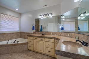 Bathroom featuring tiled tub, vanity, and tile patterned floors