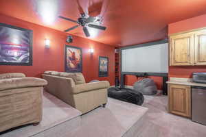 Carpeted cinema room with ceiling fan