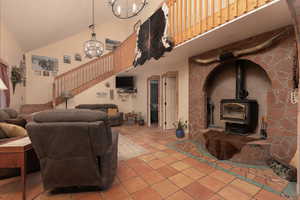 Tiled living room with high vaulted ceiling, a chandelier, and a wood stove