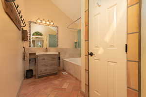 Bathroom featuring vanity, tiled bath, and vaulted ceiling