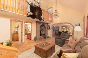 Tiled living room featuring a wood stove, high vaulted ceiling, and a notable chandelier