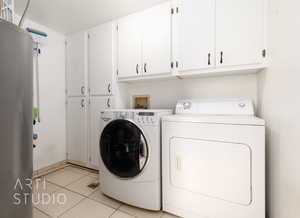 Clothes washing area with washing machine and dryer, cabinets, and light tile patterned floors