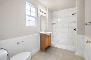 Bathroom featuring tiled shower, tile patterned floors, vanity, and toilet