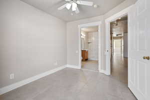 Unfurnished bedroom featuring light tile patterned flooring, ensuite bath, and ceiling fan