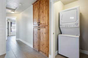 Clothes washing area featuring light tile patterned floors, stacked washer / drying machine, and a textured ceiling