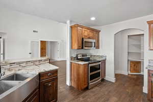 Kitchen with dark hardwood / wood-style flooring, sink, light stone countertops, appliances with stainless steel finishes, and a textured ceiling