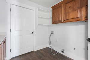 Clothes washing area featuring dark wood-type flooring, washer hookup, and cabinets