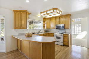 Kitchen featuring sink, light hardwood / wood-style floors, kitchen peninsula, and white range with gas cooktop