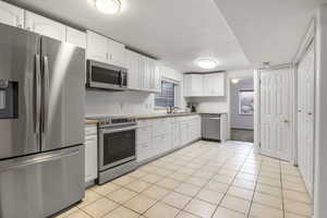 Kitchen with a textured ceiling, sink, white cabinetry, stainless steel appliances, and light tile patterned floors