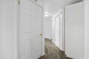 Corridor featuring a textured ceiling and dark colored carpet