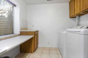 Laundry room featuring washer and clothes dryer, cabinets, and light tile patterned floors