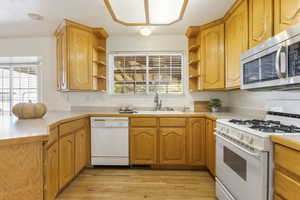 Kitchen with light hardwood / wood-style floors, white appliances, and sink