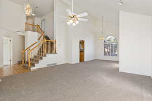 Unfurnished living room featuring high vaulted ceiling, ceiling fan with notable chandelier, and carpet floors