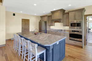 Kitchen with light wood-type flooring, a breakfast bar, a large island with sink, sink, and stainless steel appliances