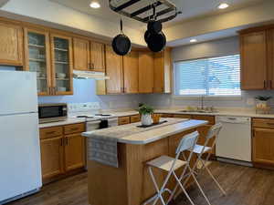 Kitchen with sink, white appliances, dark wood-type flooring, a center island, and a kitchen bar