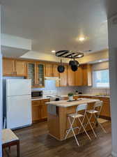 Kitchen with sink, white appliances, dark wood-type flooring, a center island, and a kitchen bar