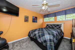 Carpeted bedroom featuring ceiling fan and a textured ceiling