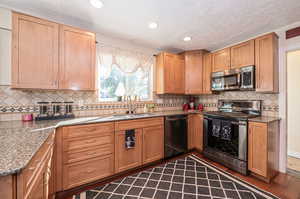 Kitchen featuring appliances with stainless steel finishes, stone counters, sink, and hardwood flooring