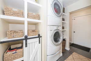 Clothes washing area with stacked washer / drying machine and dark tile patterned floors