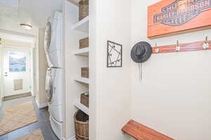 Clothes washing area featuring a textured ceiling, stacked washing maching and dryer, and dark tile patterned floors