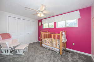 Carpeted bedroom with a crib, a textured ceiling, a closet, and ceiling fan