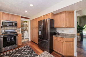 Kitchen featuring stone countertops, a textured ceiling, stainless steel appliances, and hardwood flooring