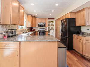 Kitchen with light hardwood floors, light stone counters, light brown cabinets, stainless steel appliances, and sink