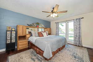 Owner's Suite featuring ceiling fan, a textured ceiling, wooden walls, and dark wood-type flooring