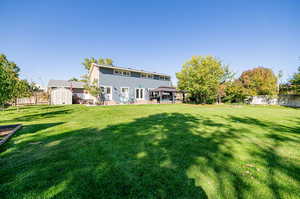 Rear view of property featuring a storage shed, a lawn, and a patio area