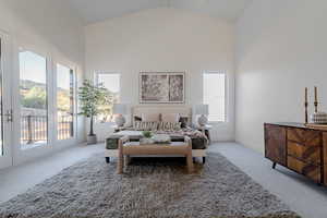 Primary bedroom with access to outside, carpet, multiple windows, and high vaulted ceiling