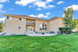 Back of property with a patio, a balcony, a lawn, and central AC unit