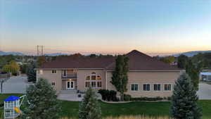 Back house at dusk with a patio, a yard, a balcony, and a mountain view