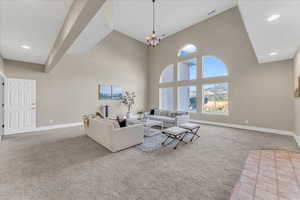 Carpeted living room featuring a notable chandelier and a towering ceiling