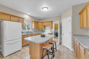 Kitchen featuring light brown cabinets, a textured ceiling, white appliances, and a kitchen island