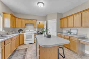 Kitchen with a kitchen island, sink, white range with electric cooktop, a kitchen breakfast bar, and a textured ceiling