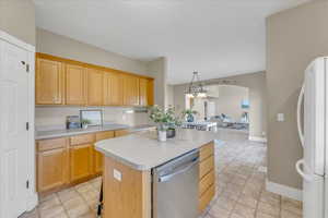 Kitchen featuring pendant lighting, a kitchen island, light brown cabinets, white fridge, and stainless steel dishwasher