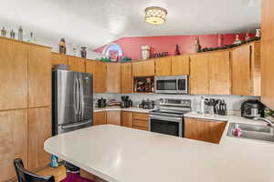 Kitchen with hardwood / wood-style floors, vaulted ceiling, sink, stainless steel appliances, and kitchen peninsula