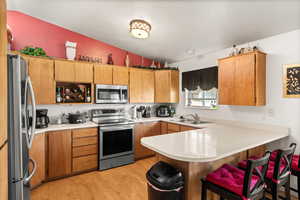 Kitchen with light wood-type flooring, vaulted ceiling, sink, stainless steel appliances, and kitchen peninsula