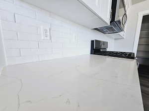 Kitchen with light stone countertops, hardwood / wood-style floors, range with gas cooktop, and white cabinets