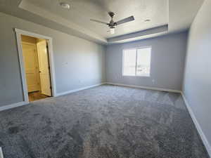 Unfurnished room with ceiling fan, a tray ceiling, carpet, and a textured ceiling