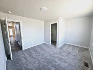 Unfurnished bedroom with a closet, dark carpet, a walk in closet, and a textured ceiling