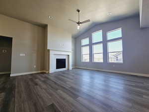 Unfurnished living room featuring ceiling fan, a textured ceiling, dark hardwood / wood-style floors, a tile fireplace, and vaulted ceiling