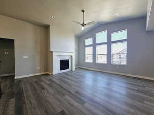 Unfurnished living room featuring ceiling fan, lofted ceiling, a brick fireplace, a textured ceiling, and dark hardwood / wood-style floors