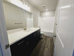 Full bathroom featuring hardwood / wood-style flooring, vanity, shower / bathtub combination, and toilet