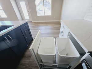 Kitchen featuring a healthy amount of sunlight, light stone countertops, wood-type flooring, and blue cabinetry